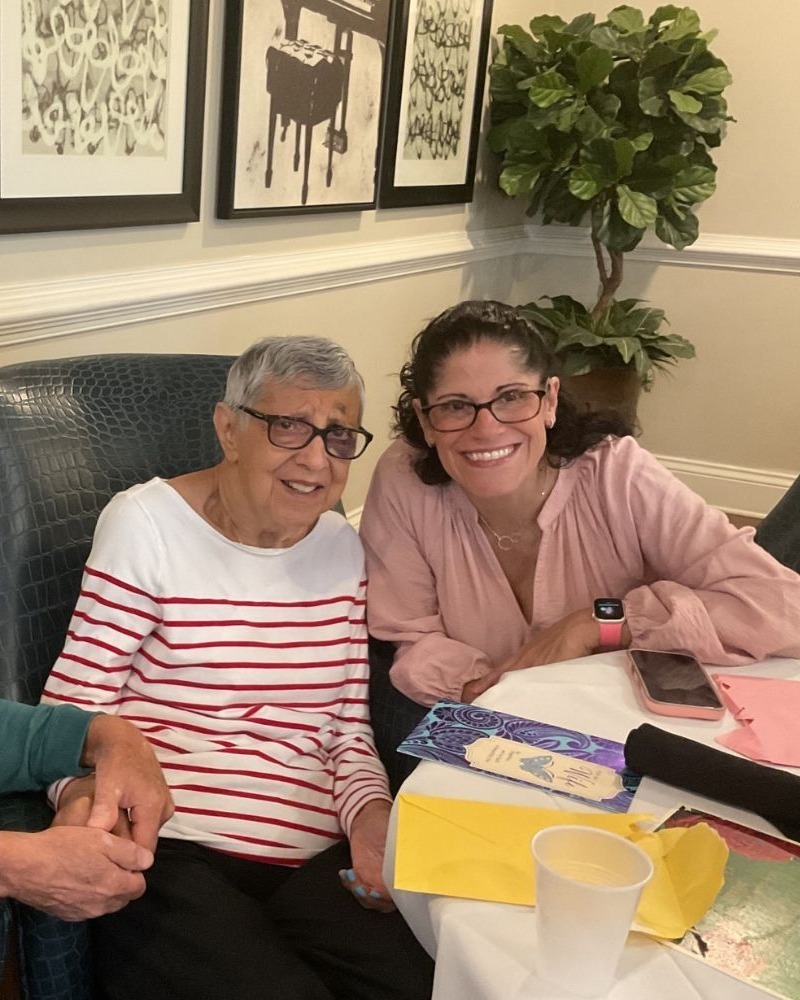 Two women share a warm smile in the inviting dining room at Arbor Terrace South Forsyth, reflecting the close-knit community feel of senior living in Suwanee, GA.