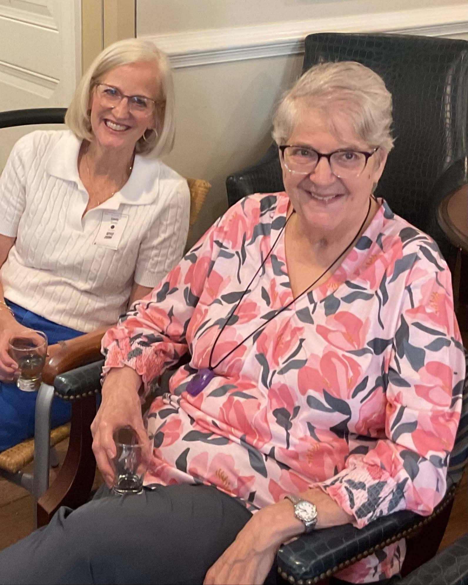 Two women relax and smile together in a cozy seating area at Arbor Terrace South Forsyth, enjoying the warm, welcoming community atmosphere of senior living in Suwanee, GA.