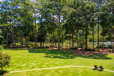 A sweeping lawn bordered by tall pines and a peaceful lake view near Arbor Terrace South Forsyth, reflecting the nature-focused senior living environment close to Suwanee, GA.