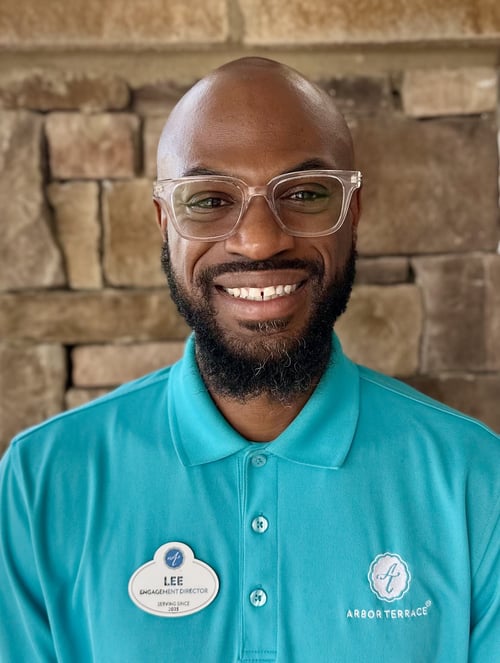A staff member in a teal polo and name badge smiles for a professional headshot at this senior living community in Suwanee, GA.