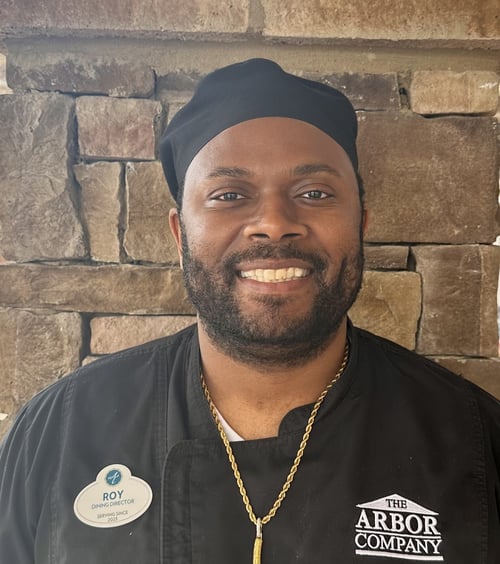 A staff member in an Arbor Company shirt smiles confidently for a professional headshot at Arbor Terrace South Forsyth assisted living.
