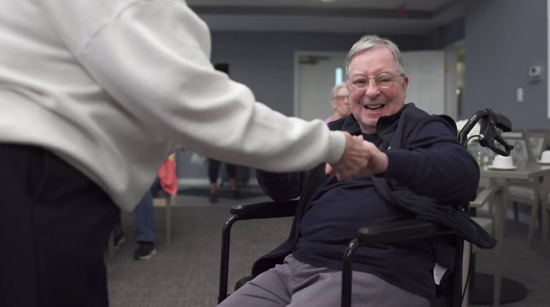 Smiling resident in wheelchair, holding hands