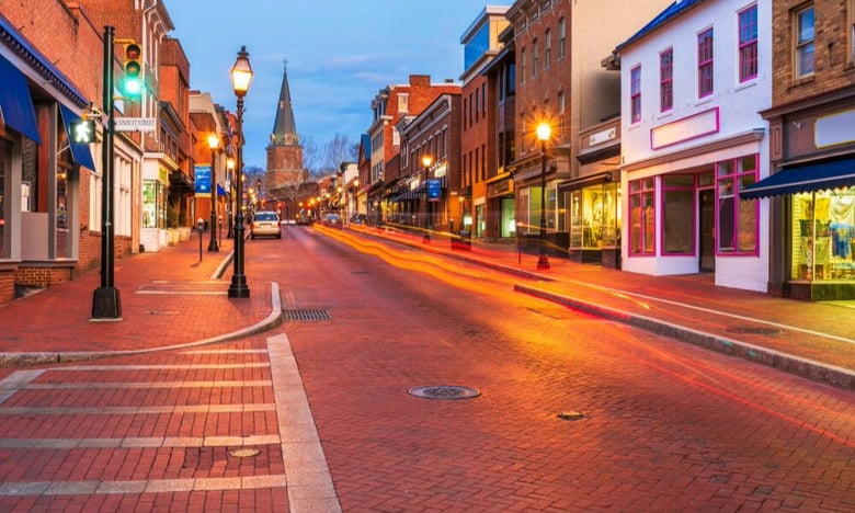 A charming small-town street glows at dusk with historic buildings, string lights, and a distant steeple, reflecting the welcoming feel that assisted living Dale City VA families find near senior living Woodbridge VA.