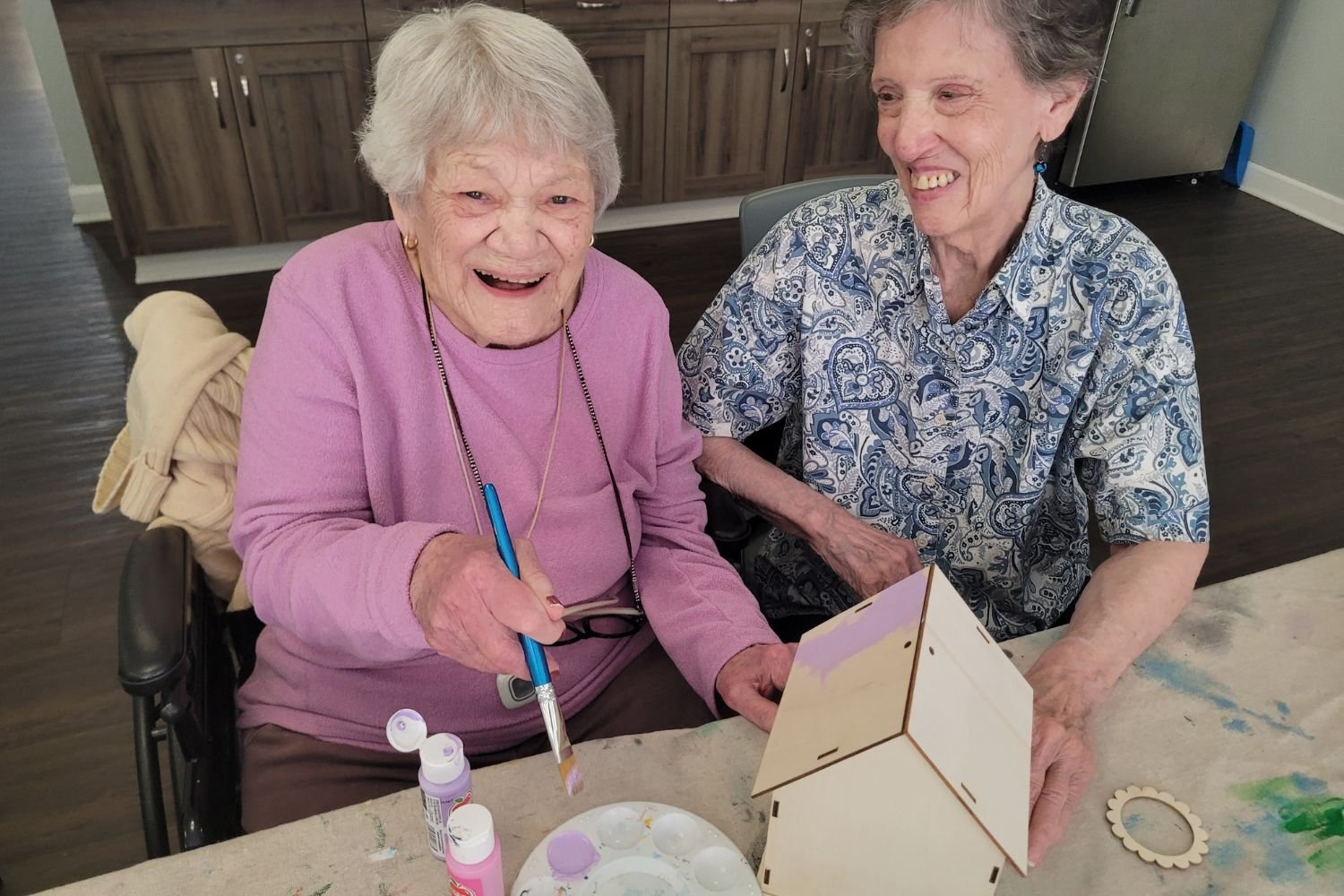 two women paint birdhouses and smile