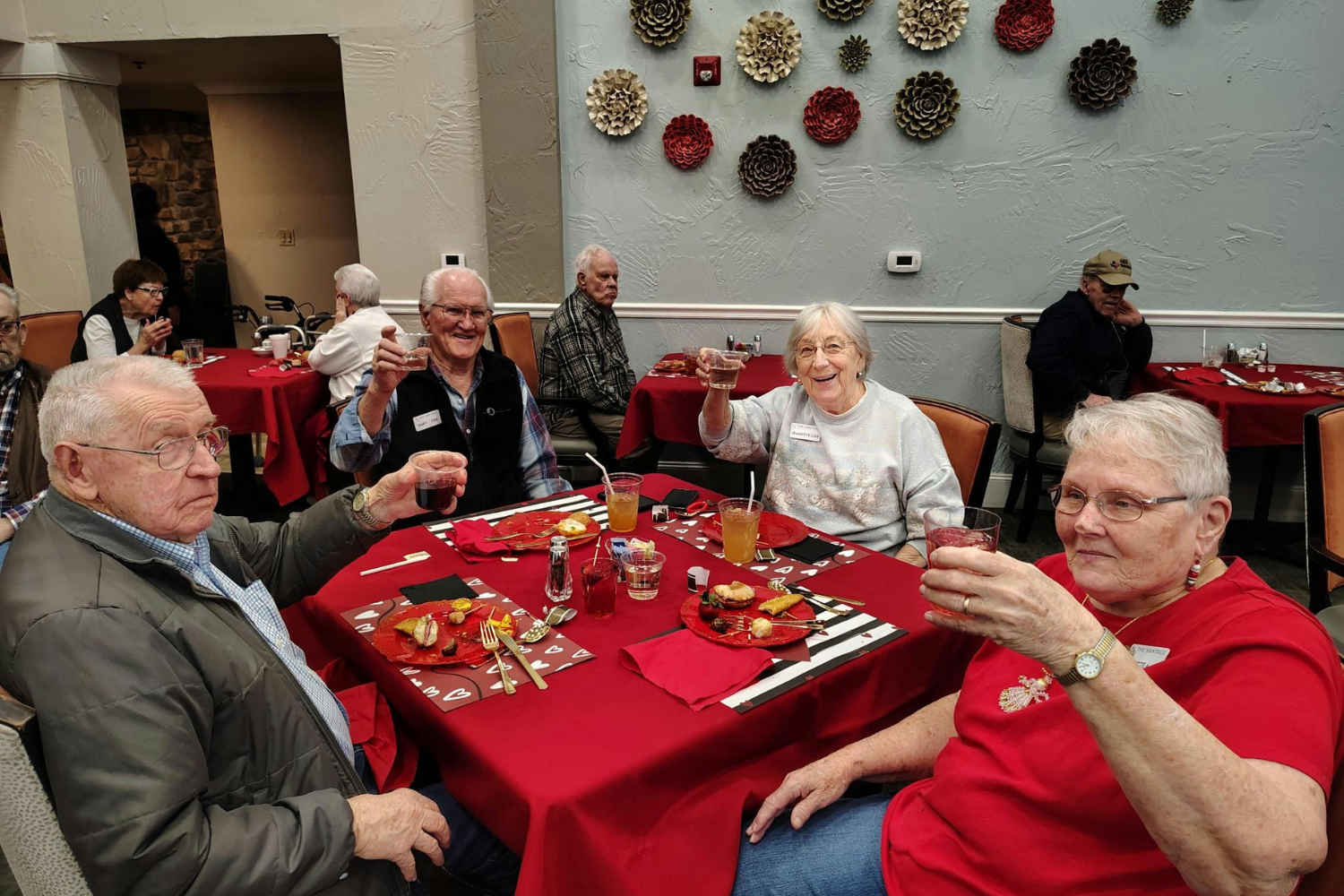 Residents sitting at a table with a red tablecloth at a holiday party toasting in celebration