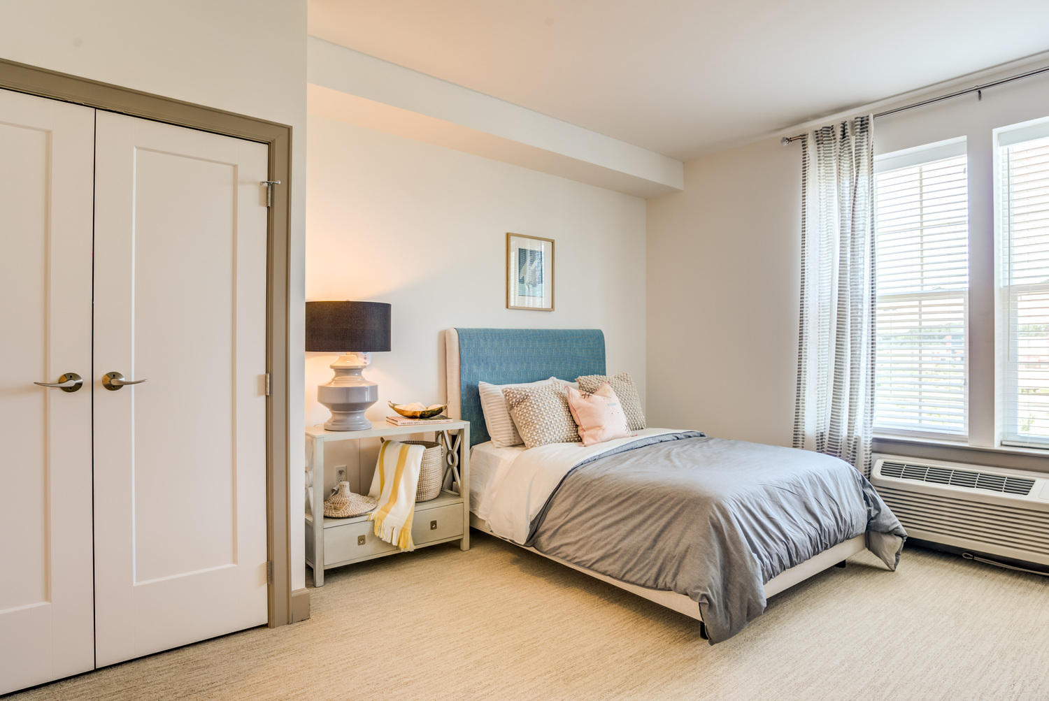 A bright and spacious apartment bedroom at Arbor Terrace Waugh Chapel featuring large windows, a tufted headboard, and soft neutral tones, reflecting the comfortable, home-like living spaces offered at this senior living community in Gambrills, MD.