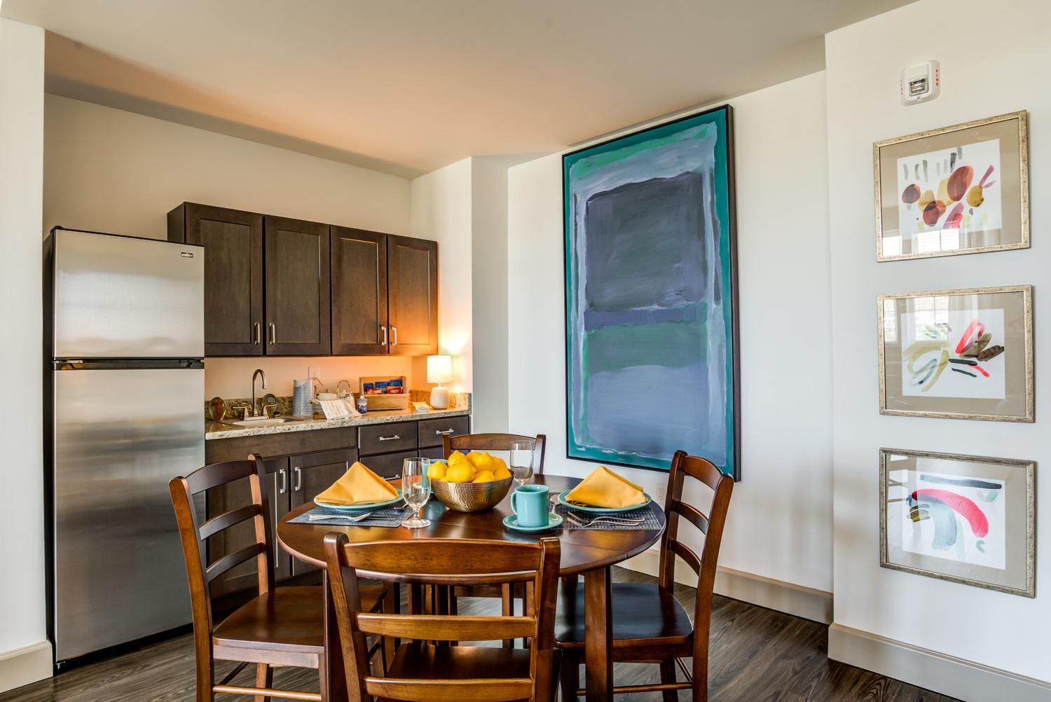 A cozy apartment dining area at Arbor Terrace Waugh Chapel featuring a wooden table, cushioned chairs, and an open kitchen, reflecting the comfortable and well-designed living spaces available at this senior living community in Gambrills, MD.