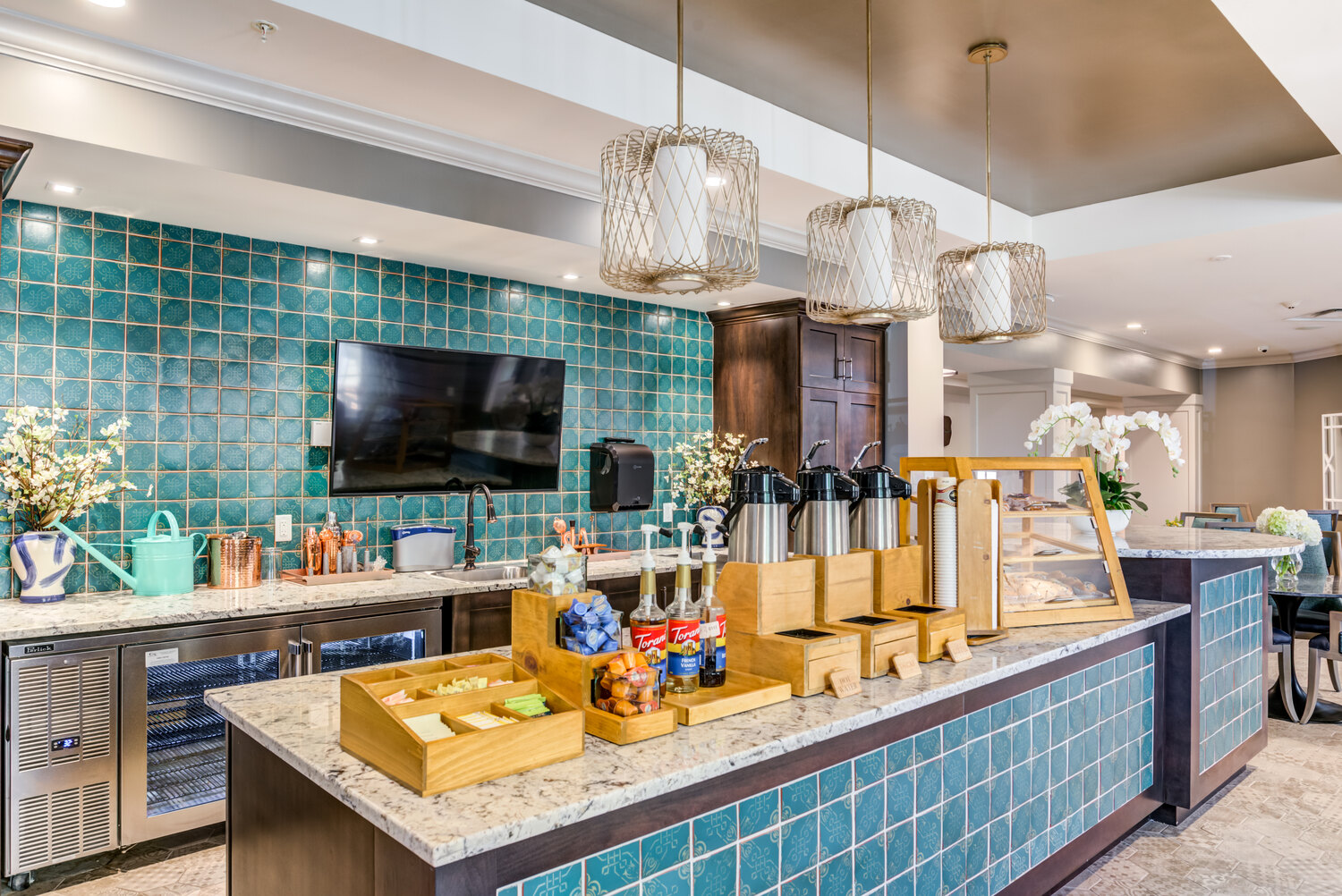 A vibrant community bar and lounge area at Arbor Terrace Waugh Chapel featuring teal tile accents, warm pendant lighting, and thoughtful décor, highlighting the engaging and upscale senior lifestyle amenities at this Gambrills, MD community.