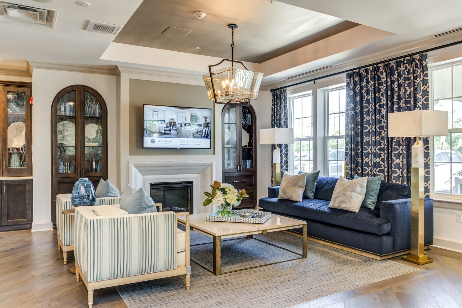 Sitting area with a navy couch and striped chairs. coffee table and fire place with a chandelier above. Navy curtains hanging in the background