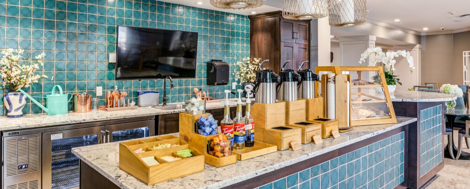 A stylish community bar and lounge area at Arbor Terrace Waugh Chapel featuring teal tile accents, wooden display elements, and warm pendant lighting, showcasing the resort-style amenities that define senior living near Waugh Chapel Towne Centre.