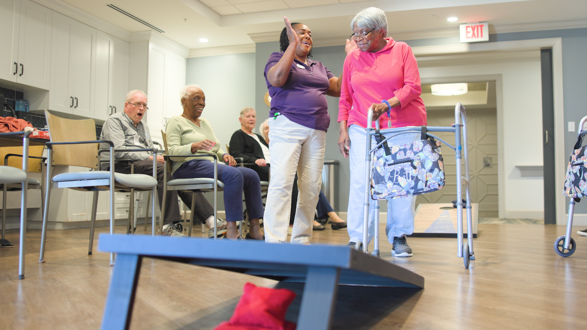 staff high fiving a senior lady in pink after winning cornhole while senior audience gasps in amazement