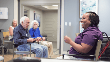 A smiling staff member engages with residents during a group activity in a bright, welcoming common area at our assisted living community in Gambrills, MD.