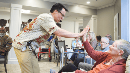 An entertainer enthusiastically high-fives a resident during a lively performance, as a crowd of residents looks on and enjoys the fun at our senior living community in Gambrills, MD.