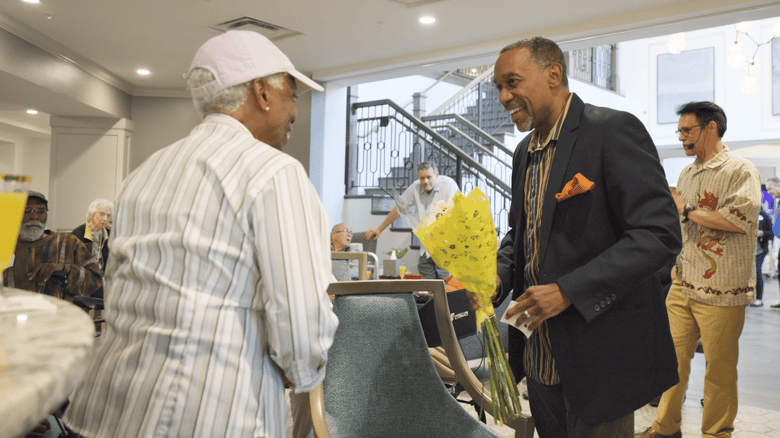 Resident in a suit giving flowers to their significant other in the common room during an entertainment event 
