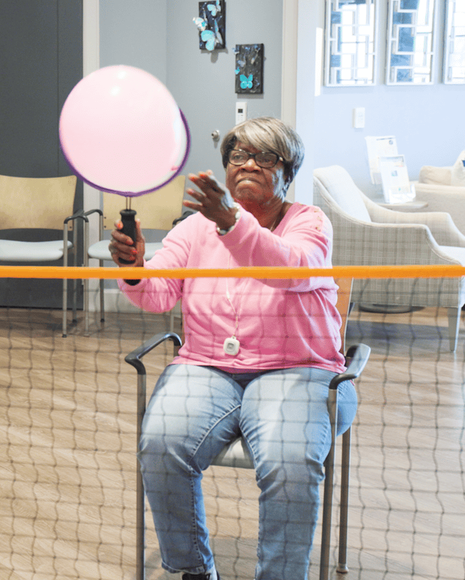A female resident enthusiastically leads a balloon activity with residents at Arbor Terrace Waugh Chapel, capturing the energetic and joyful atmosphere of the engaging senior lifestyle programs at this assisted living community in Gambrills, MD.