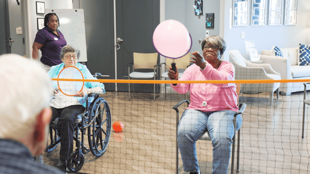 Residents enjoy a lively balloon volleyball game during an engaging senior living activity at our assisted living community in Gambrills, MD, with a staff member looking on nearby.