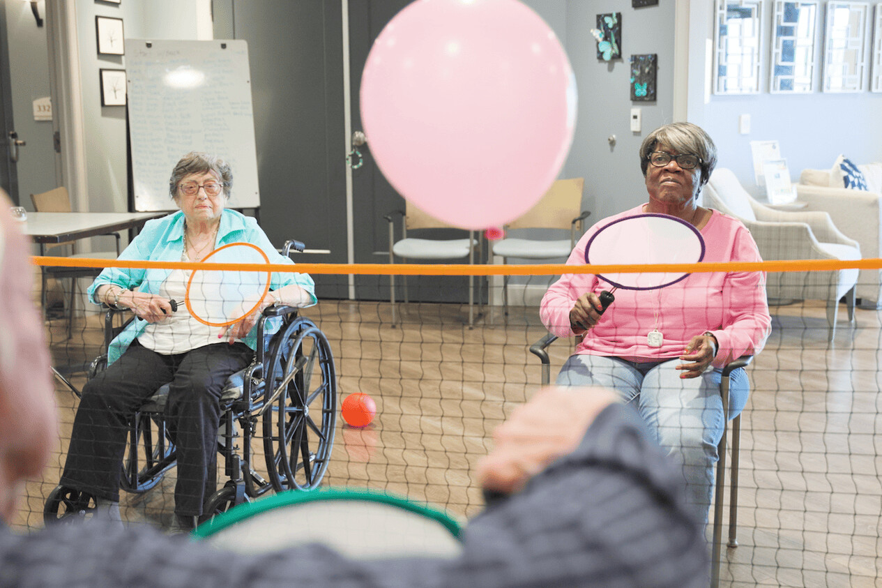 Residents enjoy a lively balloon volleyball game during an engaging senior living activity at our assisted living community in Gambrills, MD, with a staff member looking on nearby.