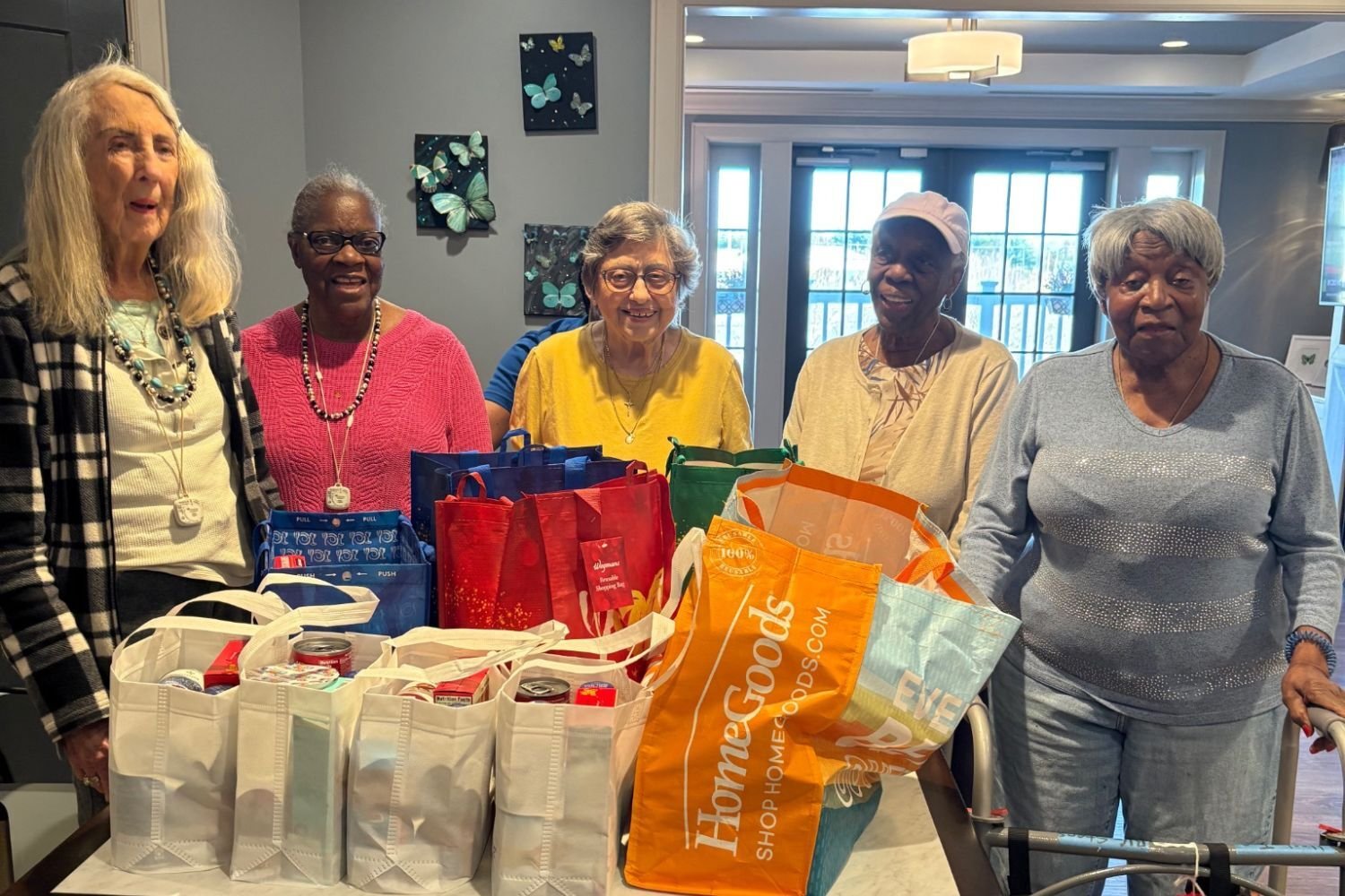 Residents and staff gather around a collection of donated groceries and goods at Arbor Terrace Waugh Chapel, reflecting the generous and community-minded spirit that makes this senior living community in Gambrills, MD a truly warm and giving place.