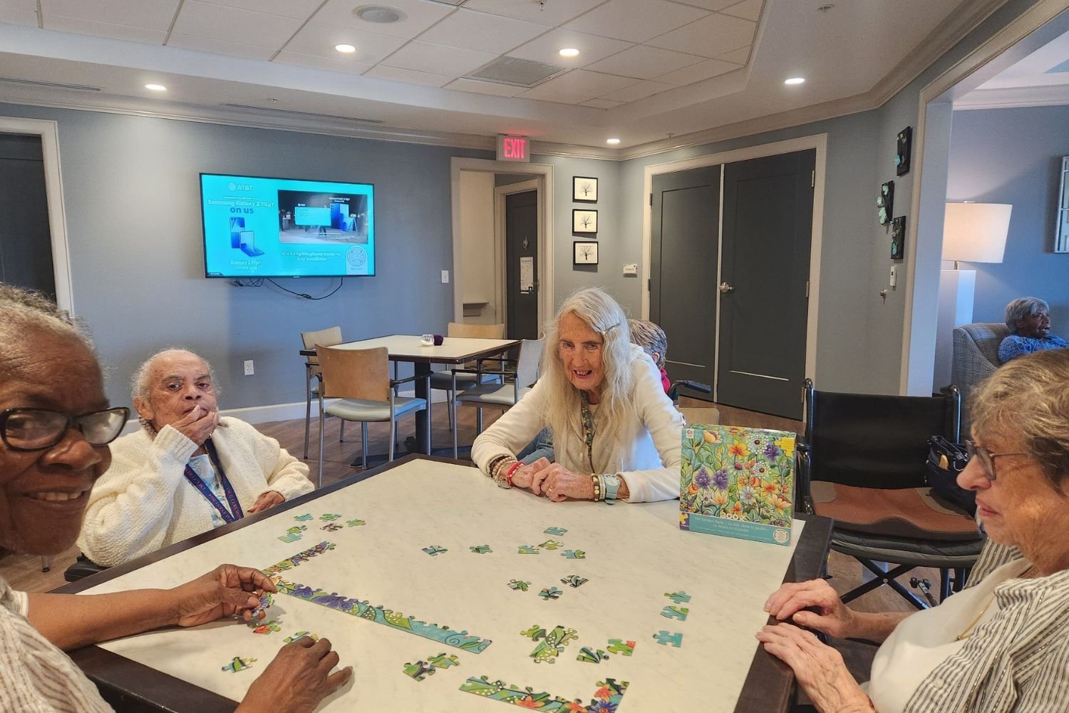 Residents work together on a puzzle around a table at Arbor Terrace Waugh Chapel, capturing the engaging and mentally stimulating lifestyle programs that support cognitive wellness at this senior living community in Gambrills, MD.