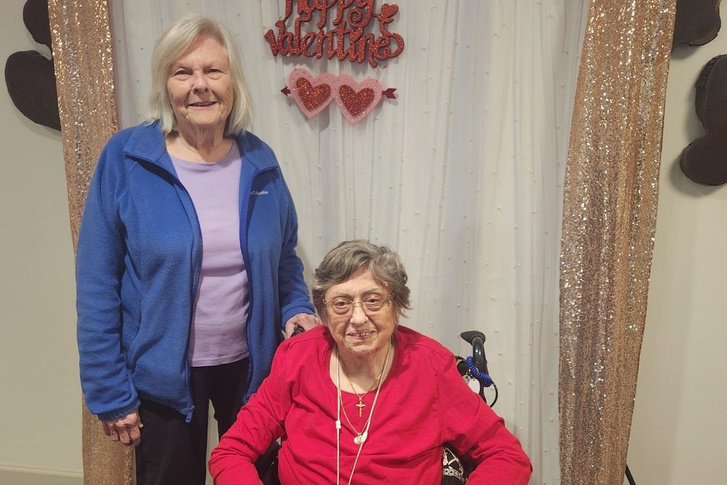 Two residents pose together with cheerful Valentine's Day decorations at Arbor Terrace Waugh Chapel, capturing the festive seasonal celebrations and warm community spirit that make this assisted living community in Gambrills, MD feel like home.