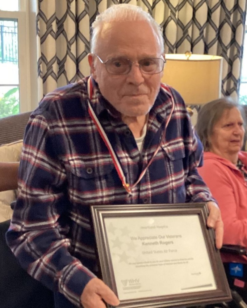 A resident proudly holds a framed veteran recognition certificate while wearing a medal at Arbor Terrace Waugh Chapel, a senior living community in Gambrills, MD that honors those who have served.