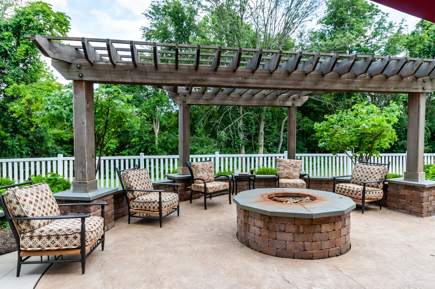 Pergola-covered outdoor seating area with a fire pit at Arbor Terrace Willistown in West Chester, PA, surrounded by trees and landscaped grounds.