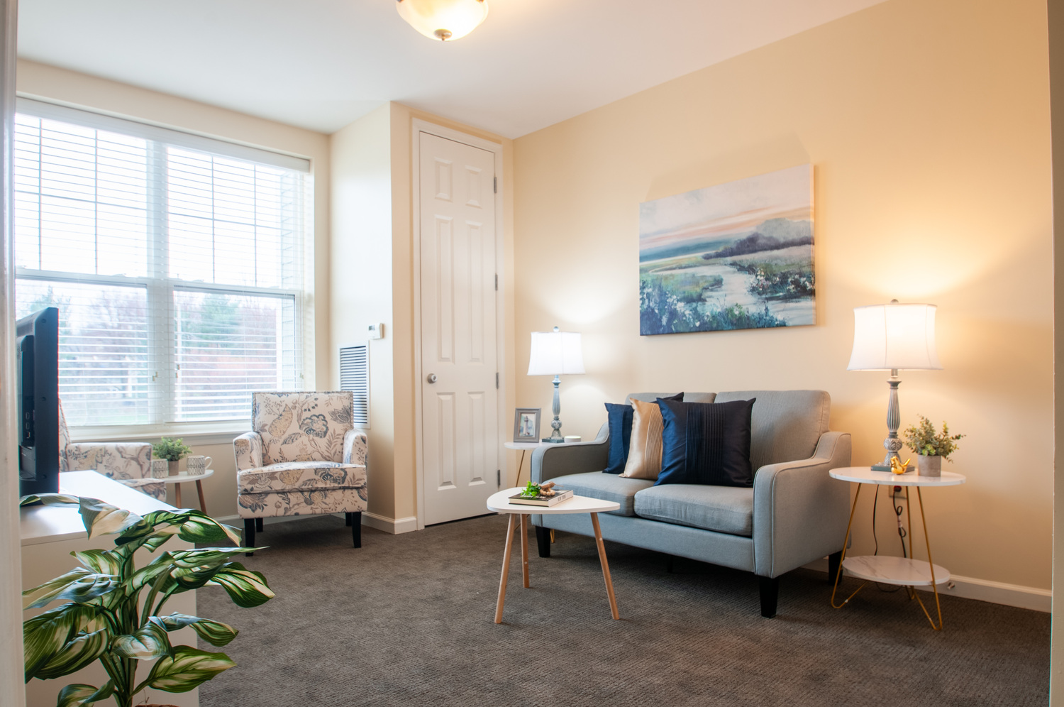 Bright senior living apartment living room at Arbor Terrace Willistown in West Chester, PA, featuring a cozy sofa, armchair, and large windows.