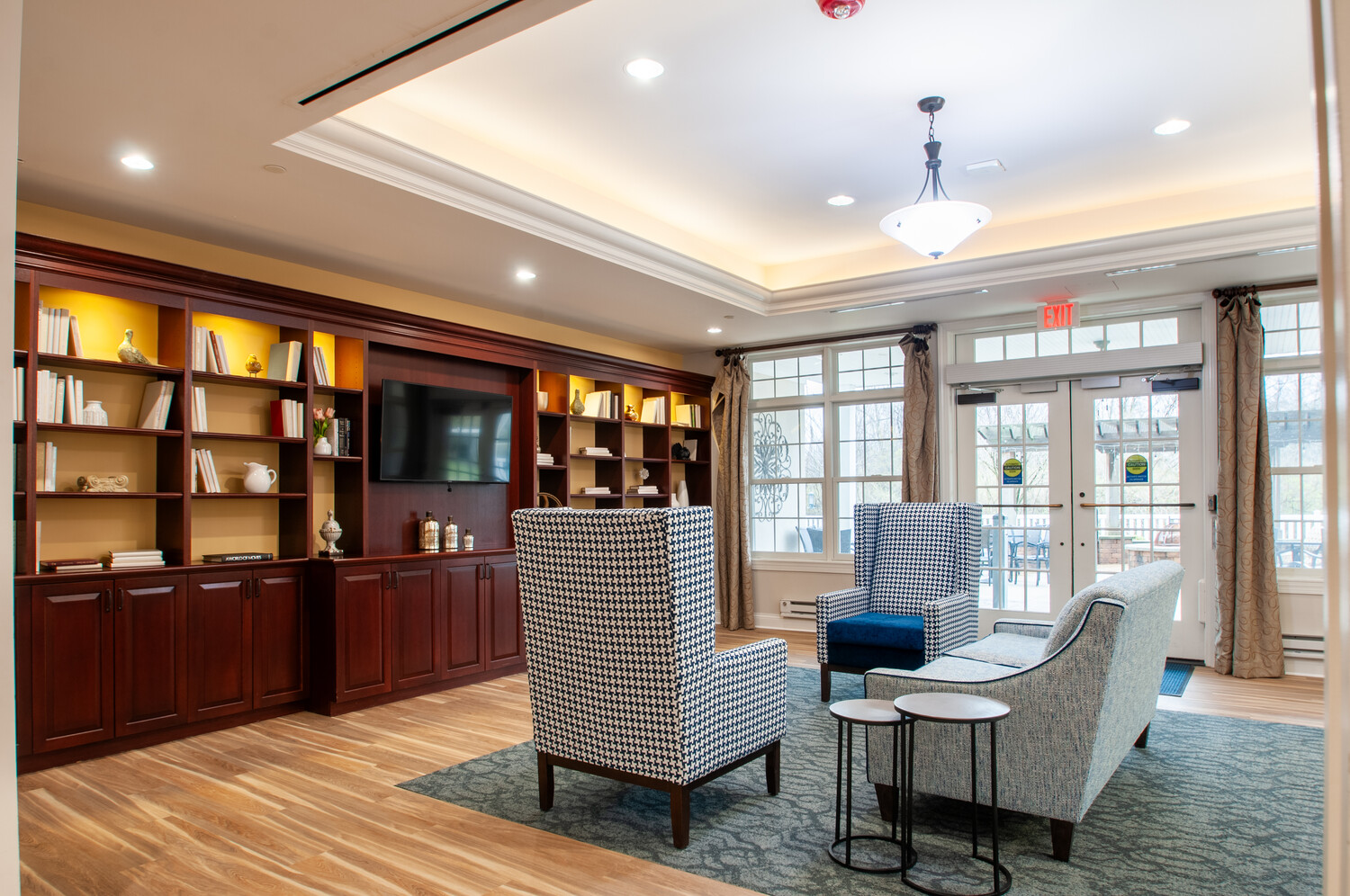 Inviting common area lounge at Arbor Terrace Willistown in West Chester, PA, featuring built-in shelving, comfortable seating, and natural light from large windows.