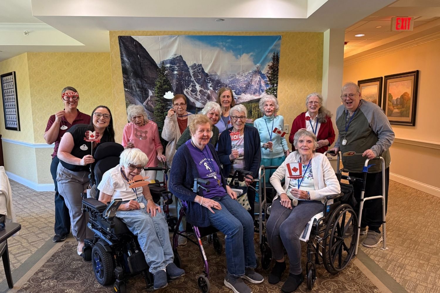 residents and employees smile and gather in front of a backdrop of a snowy mountain. some people are holding mini Canadian flags