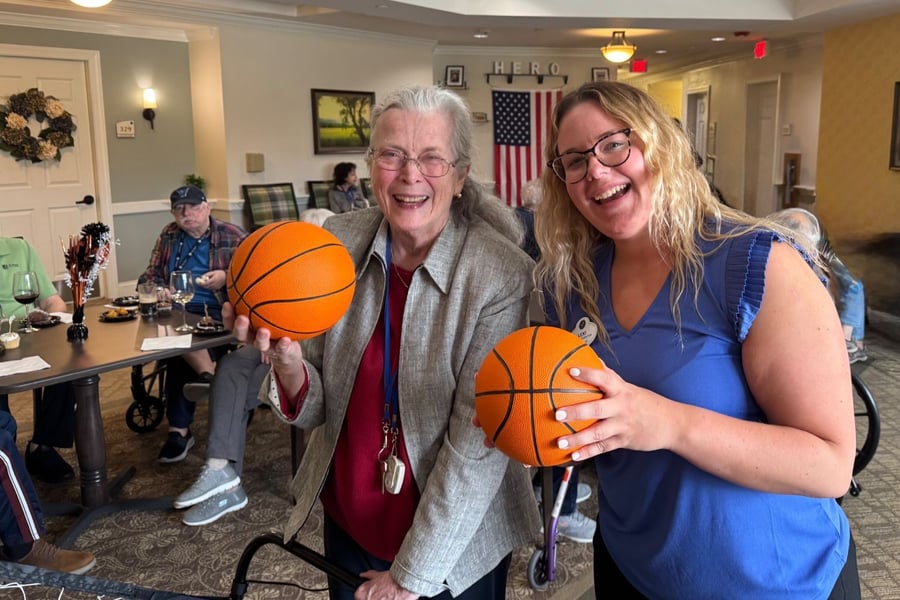 A smiling resident and team member at Arbor Terrace Willistown holding small basketballs during a fun activity, showcasing the vibrant and engaging senior living community atmosphere.