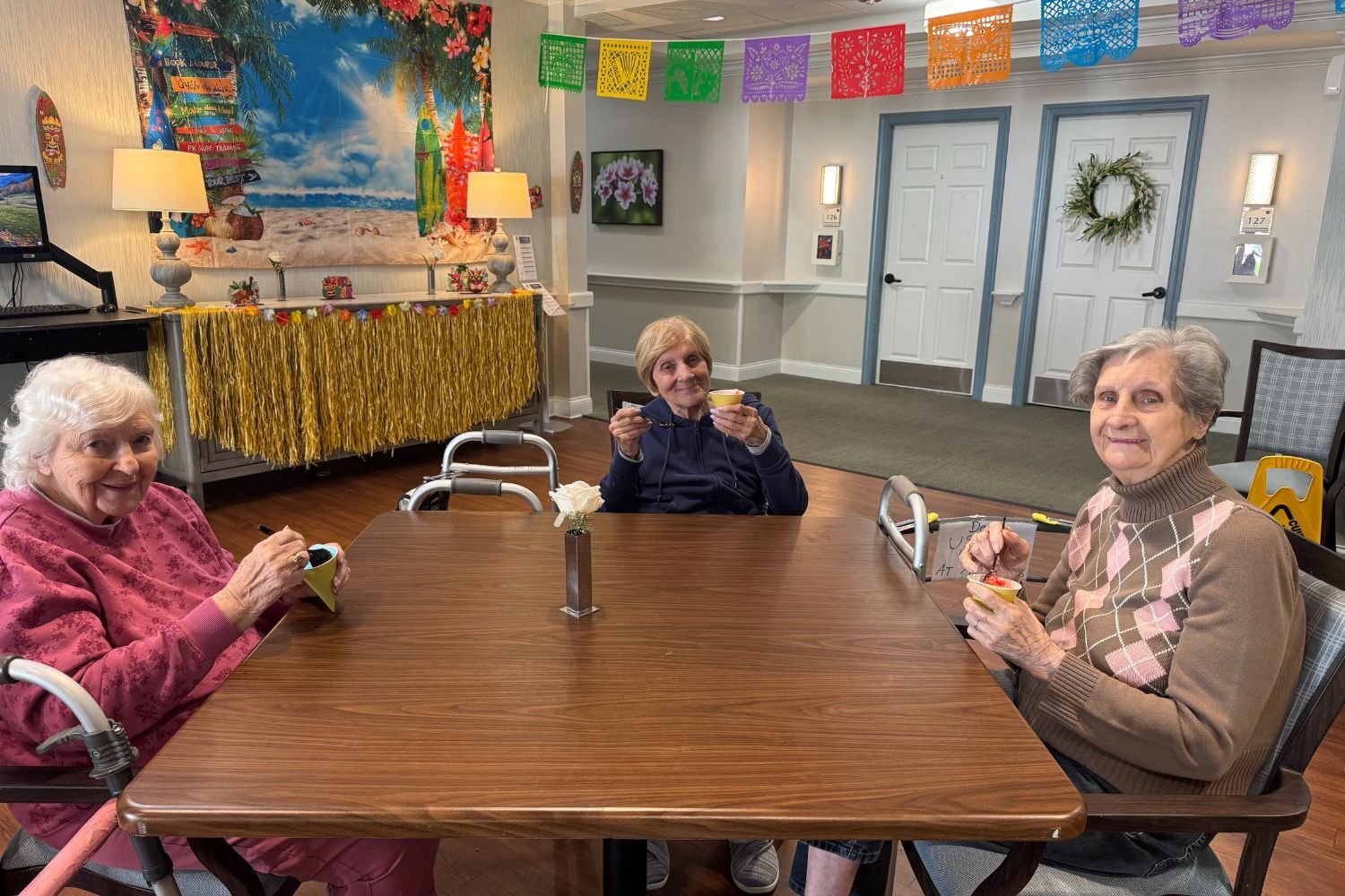 three residents/women sit around a table and smile. they are holding snow cones and spoons