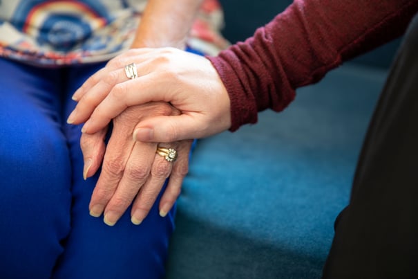 A close-up of two pairs of hands resting together on a teal cushion, capturing a tender moment of senior care in Woodbridge, VA, where compassionate support and human connection are at the heart of assisted living.