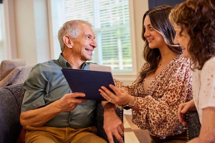 A smiling older adult sits with two younger visitors reviewing information on a tablet — personalized assisted living Lakeway TX care plans built with residents and their families.