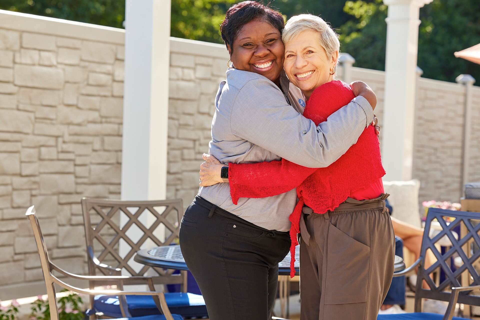 a senior lady hugging a female staff outdoors