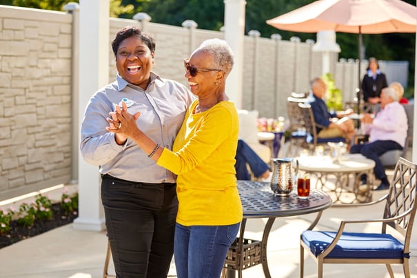 A staff member and a resident laugh and dance together on a sunny outdoor patio at Mirabelle, a vibrant senior living community in Miami, FL where joyful engagement and cognitive wellness go hand in hand.