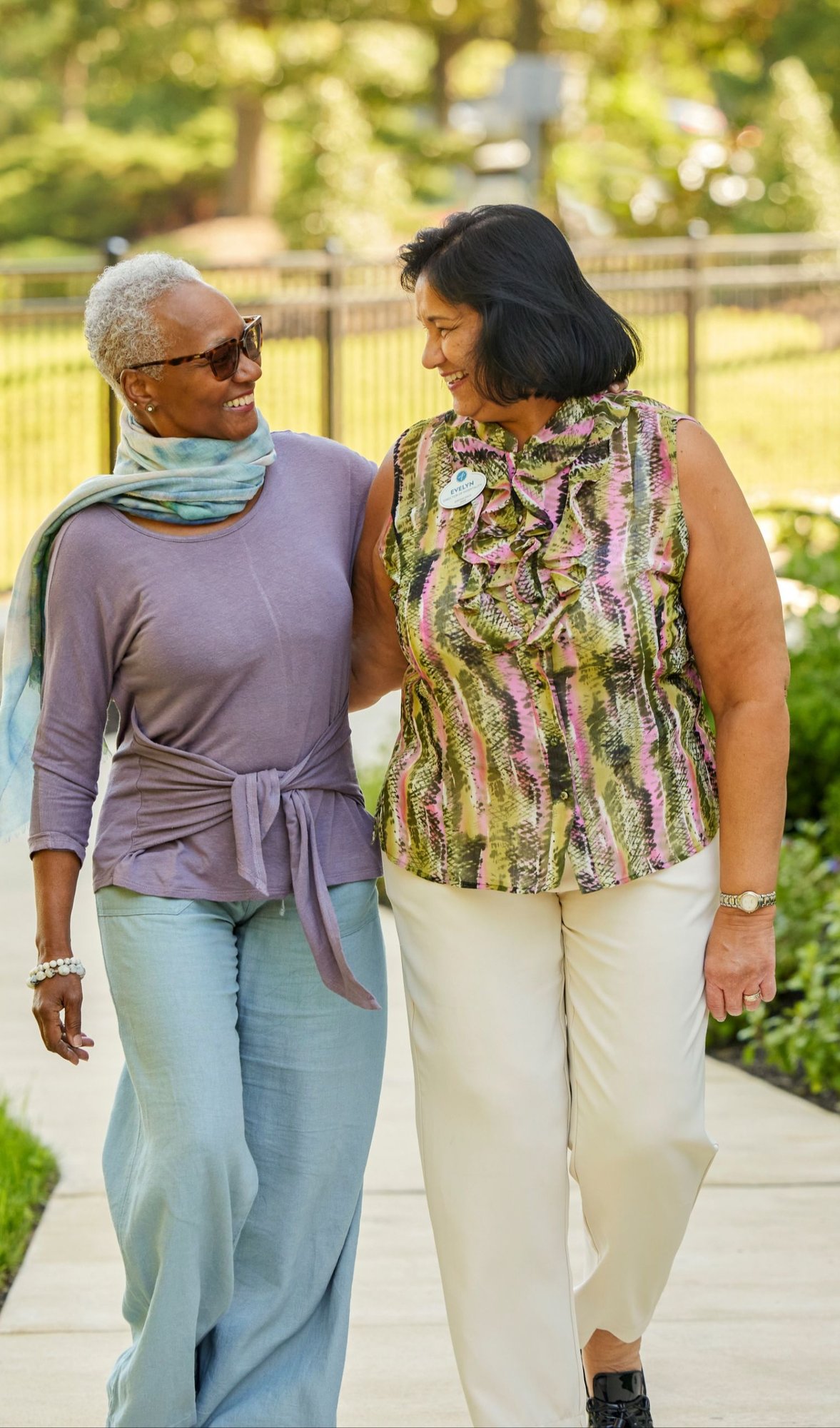 Residents and staff member walking outside on a sidewalk smiling at each other