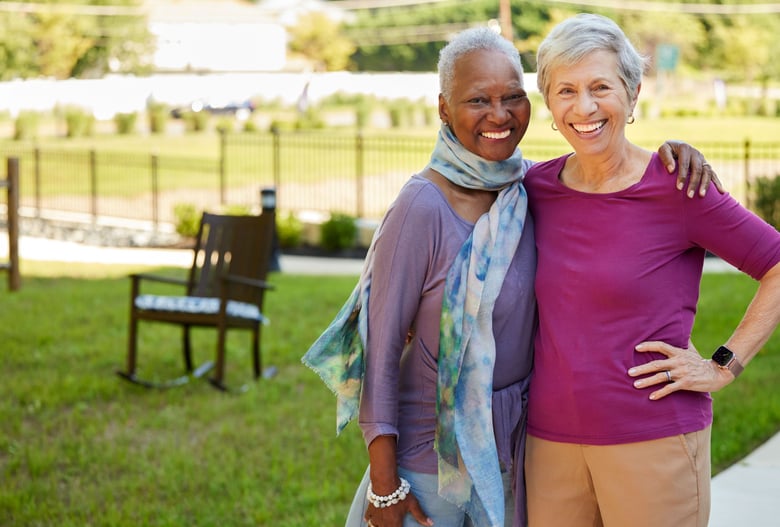 Residents smiling outside in a green area with a rocking chair in the background