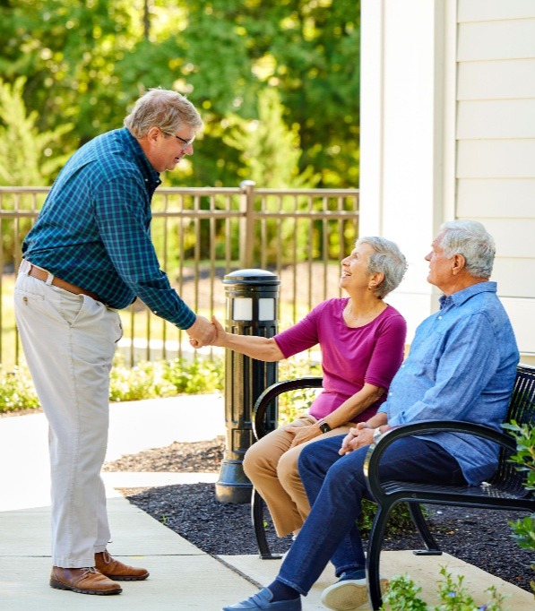 residents sitting outside on a bench shaking a third residents hand