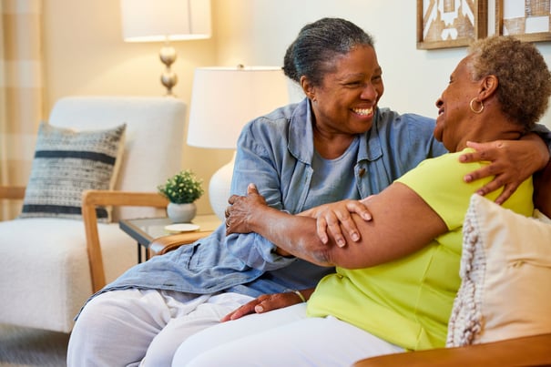 Two people share a warm, heartfelt laugh together on a cozy sofa in a bright, welcoming living space at our assisted living community in Gambrills, MD.
