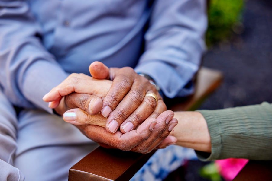 A close-up of three sets of hands gently clasped together, representing the compassionate, trust-based care offered at a memory care community in Athens, GA.