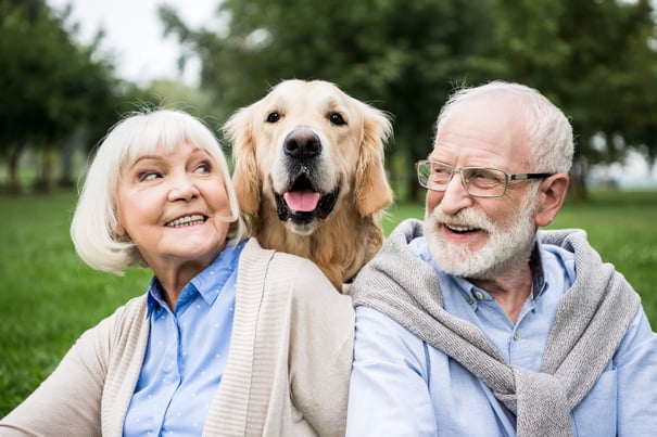 An older couple smiles warmly alongside a happy golden retriever on a green lawn, enjoying the pet-friendly senior living lifestyle available in Athens, GA.