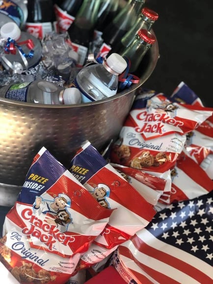 A festive spread of Cracker Jack snack bags and a metal beverage bucket set up for an Independence Day celebration at Arbor Terrace Athens, a senior living community in Athens, GA.