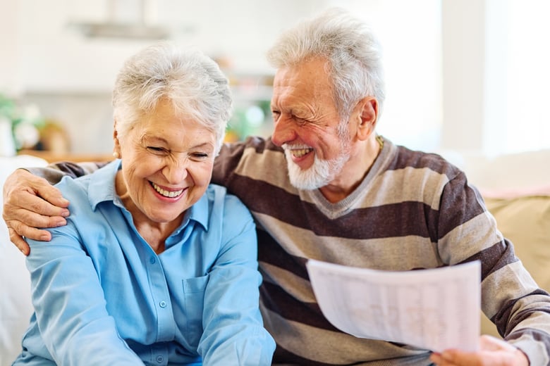 Smiling senior couple sitting together on a couch, sharing a laugh while looking over paperwork.