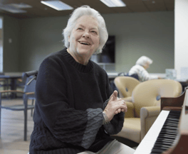 A resident smiles warmly while seated near a piano in a comfortable common area, enjoying the engaging senior lifestyle programs at this Acworth senior living community.
