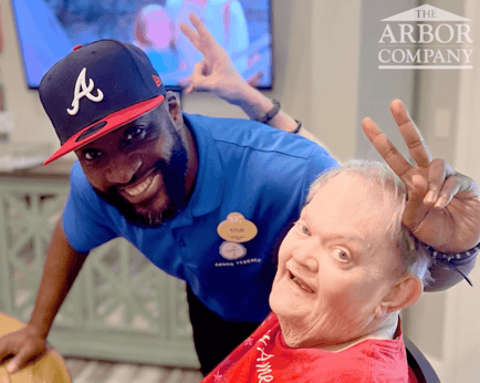 A staff member wearing an Arbor Terrace name tag and a baseball cap laughs and poses playfully with a resident at a senior living community in Athens, GA, capturing the warm, joyful spirit of the team.