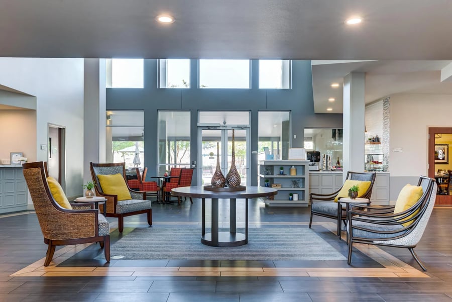 A spacious, light-filled common area at Arbor Terrace Lakeway with high ceilings, large windows, and stylish seating — exploring the cost of assisted living near Bee Cave TX.