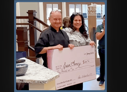 Two Arbor Terrace Morris Plains team members proudly hold an oversized check in the community's grand foyer, celebrating staff recognition and the caring culture of senior living in Morris Plains, NJ.