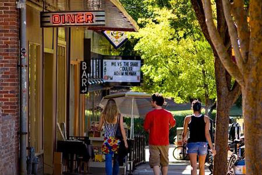 People stroll along a lively downtown Athens street lined with trees, brick storefronts, and local restaurants, steps from senior living near downtown Athens, GA.