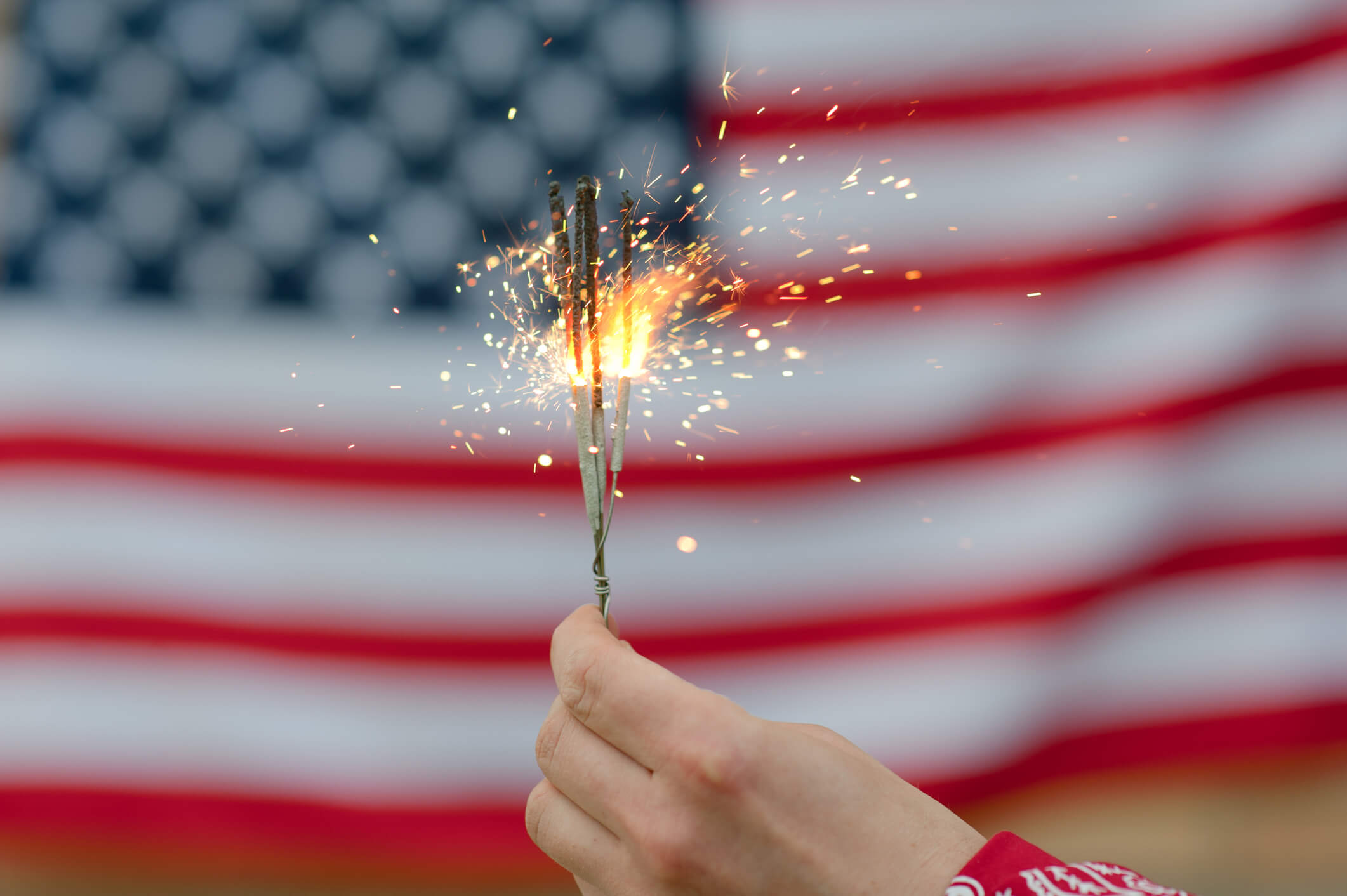 A hand holds glittering sparklers in front of an American flag, celebrating festive community traditions at senior living in Citrus Park, FL.