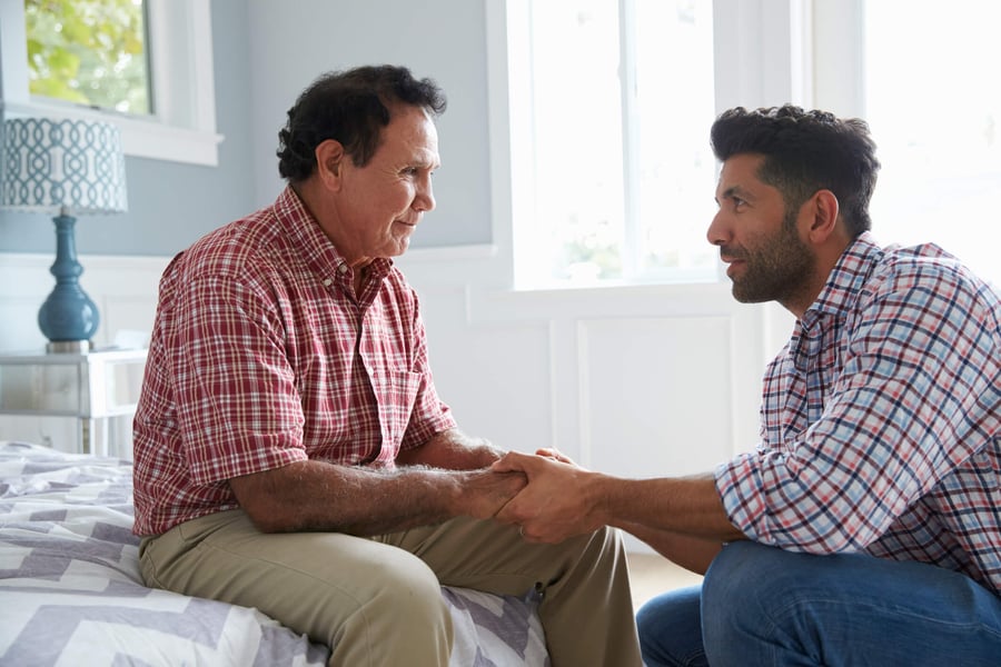 Two men sit together indoors, holding hands in a heartfelt moment of connection, reflecting the compassionate, personalized care offered at assisted living in Suwanee, GA